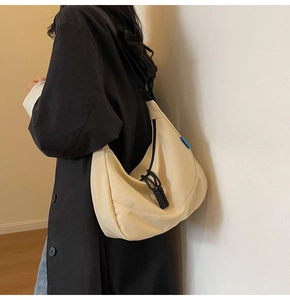 Detail of beige crescent nylon bag featuring black woven zipper and wide shoulder strap
