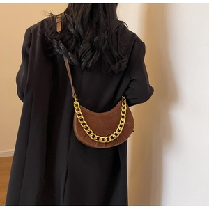 Close-up of brown suede saddle bag featuring chunky gold chain and pleated bottom detail