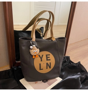 Detailed shot of dark gray tote bag with leather logo patch and yellow bird charm