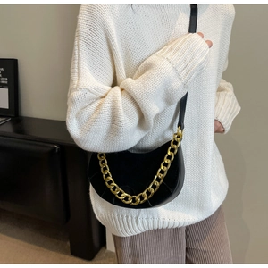 Detail of black leather saddle bag with chunky gold chain strap and curved stitching