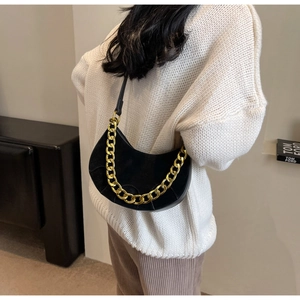 Detail of black suede half-moon saddle bag with chunky gold chain and leather strap
