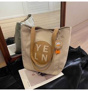 Detail of beige nylon tote bag with leather patch, featuring a cute yellow plush duck charm