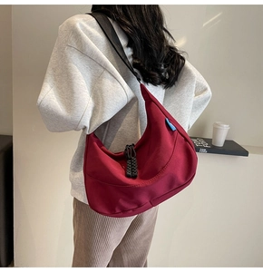 Detail of burgundy nylon crescent crossbody bag with thick black strap and woven drawstring