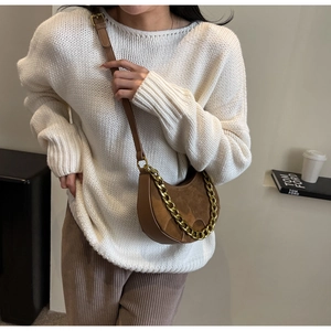 Close-up of brown suede saddle bag with chunky gold chain and leather shoulder strap