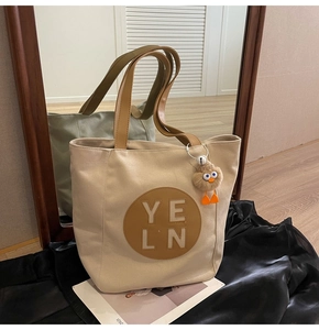 Detail of canvas tote bag with brown PU handles and yellow plush charm on black satin