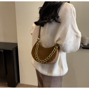 Close-up of brown suede hobo bag featuring a decorative gold chain strap on model