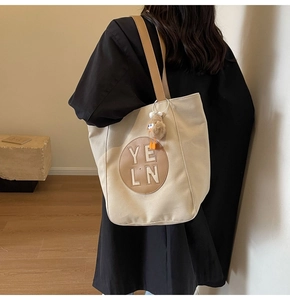 Close-up of minimalist tote bag with leather strap, logo emblem and plush charm