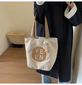 Detail of minimalist beige canvas tote bag with brown leather handles and duck pendant