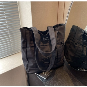 Dettaglio della borsa tote in nylon nero con ampi manici e fibbia metallica a D