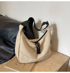 Detail of beige nylon crescent bag with black wide strap and woven zipper pull