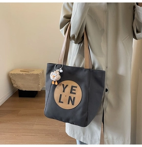 Close-up of black canvas tote bag with leather logo patch and yellow bird charm