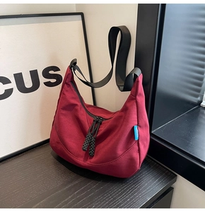 Detail of burgundy canvas hobo bag with black nylon strap and textured fabric