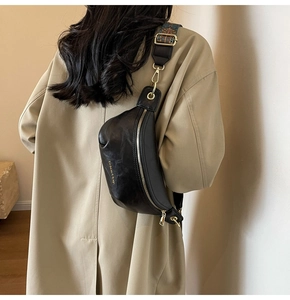 Detail of black leather crescent bag with retro patterned strap on a khaki coat