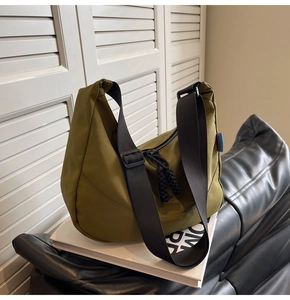 Detail of army green nylon crescent bag with adjustable black strap on a sofa