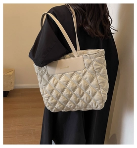 Detail of beige quilted tote bag showing rhombus stitching and brand logo patch