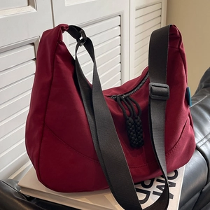 Large burgundy nylon crescent shoulder bag with wide strap on a minimalist book base