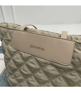 Close-up of khaki quilted tote bag featuring a leather logo patch and stitched texture