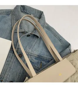 Detail of a cream faux leather tote bag with slim shoulder straps and yellow logo design