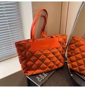 Detail of orange quilted tote bag with diamond pattern and leather logo patch