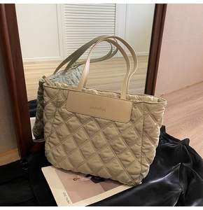 Detail of quilted diamond pattern tote bag with leather handles and brand patch