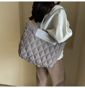 Close-up of a grey quilted tote bag featuring detailed stitching and a stylish brand flap