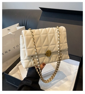 Close-up of quilted cream crossbody bag with gold twist lock and chain in a gift box