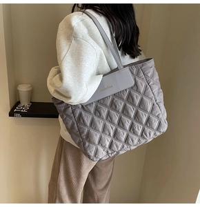 Detail of grey quilted tote bag with diamond pattern stitching and leather brand tag
