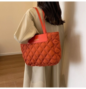 Close-up of orange quilted tote bag on shoulder showing large capacity and rhomboid texture