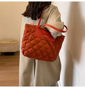 Detailed side view of large orange quilted tote bag worn by model with trench coat