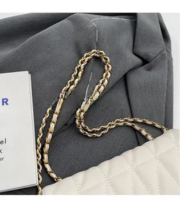 Detail of white quilted leather texture and golden woven chain strap on a flap bag