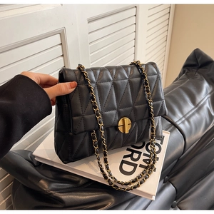 Detail of black quilted leather shoulder bag featuring gold chain strap and metal twist lock