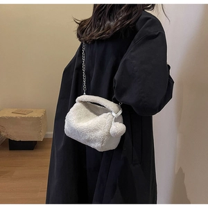 Détail du sac polochon blanc pelucheux avec chaîne argentée sur tenue noire