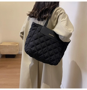 Close-up of a black quilted tote bag with diamond pattern worn over a beige coat