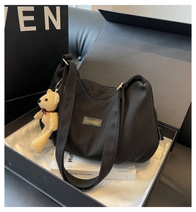 Detail of black nylon crossbody bag with BANATU logo and cute teddy bear charm