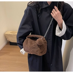 Détail d'un sac bandoulière marron en peluche avec chaîne sur un manteau noir