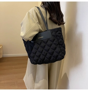 Detail of black quilted tote bag with diamond pattern and brand leather patch
