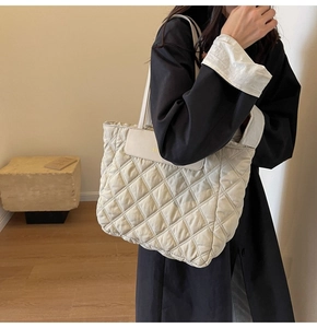 Close-up of beige quilted tote bag with diamond pattern and leather flap detail