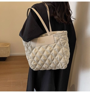 Detail of a cream quilted tote bag with diamond pattern and gold logo on the front