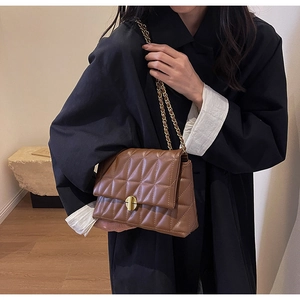 Close-up of brown quilted leather texture and gold circular twist lock on a shoulder bag