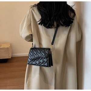 Borsa a tracolla trapuntata nera con patta ondulata indossata da modella in trench