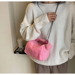Vue détaillée d'un sac en peluche rose avec chaîne argentée sur un pull blanc crème