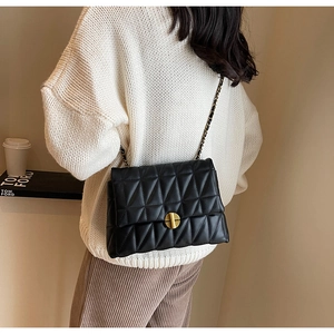 Close-up of quilted black crossbody bag with gold round turn-lock and chain strap