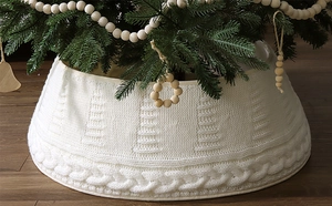 Detail der weißen Strick-Weihnachtsbaumscharpe mit Zopfmuster auf dunklem Holzboden