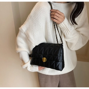 Close-up of black quilted leather shoulder bag with gold metal clasp on white sweater