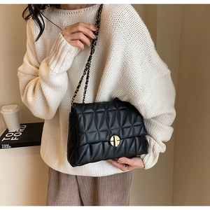 Detail of black quilted crossbody bag with golden chain strap and round metal lock