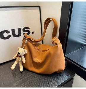 Close-up of brown canvas dumpling bag featuring leather brand tag and teddy bear charm