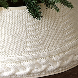 Detailaufnahme der weißen gestrickten Weihnachtsbaumdecke mit dicker Wolltextur und Mustern