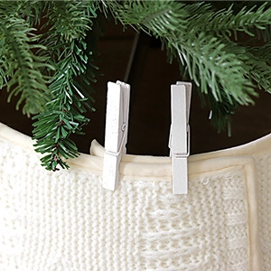 Detail of white knitted Christmas tree skirt featuring clip fasteners on green pine needles