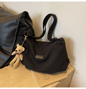 Macro detail of black corduroy hobo bag featuring a leather brand tag and plush bear charm