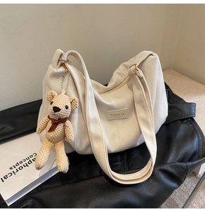 Detail showing white corduroy tote texture with leather brand label and a cute bear charm